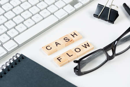 Cash flow statement concept with letters on wooden cubes. Still life of office workplace with supplies. Flat lay white surface with computer keyboard and notepad. Budget planning, audit and accountingの写真素材