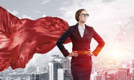 Young confident businesswoman wearing red cape against modern city backgroundの写真素材