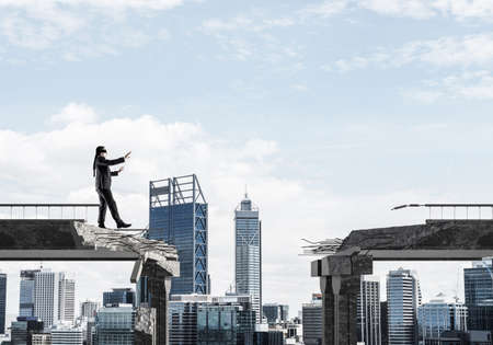 Businessman walking blindfolded on concrete bridge with huge gap as symbol of hidden threats and risks. Cityscape view on background. 3D rendering.の写真素材