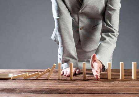 Businesswoman interrupting domino effect by stop falling wooden dominoes. Operative business solution, strategy and successful intervention. Business assistance, protection and prevention of crisisの写真素材