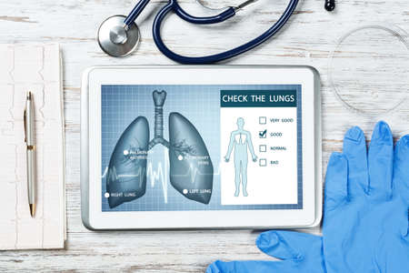 Medical diagnostics in modern pulmonology. Tablet computer with medical application interface on screen. Top view stethoscope and cardiogram on wooden desk. Digital tuberculosis screening testの写真素材