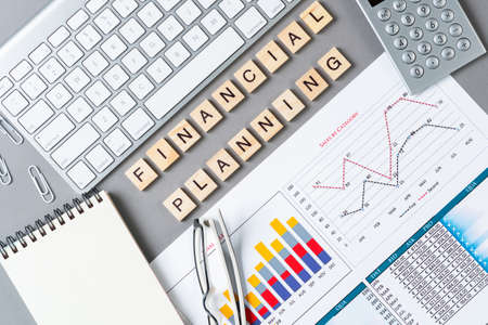 Financial planning concept with letters on cubes. Still life of office workplace. Flat lay grey surface with computer keyboard, calculator and analytic report. Company development and consulting.の写真素材