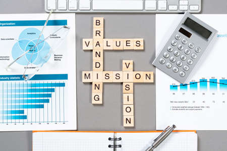 Brand value concept with words from cubes. Still life of office workplace with crossword. Flat lay grey surface with computer keyboard and calculator. Strategy planning and business management.の写真素材