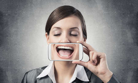 Portrait of young woman covering her mouth with smartphone.の写真素材