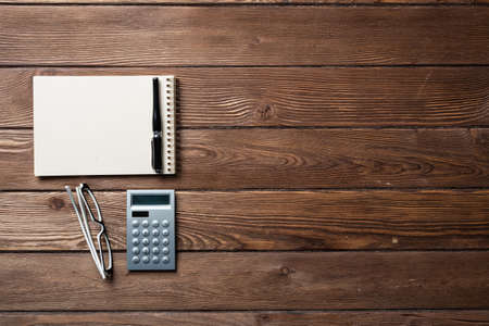 Still life of accountant workspace with office accessories. Flat lay wooden desk with elegant glasses, calculator and spiral notepad. Accounting and banking services. Finance and investment concept.の写真素材