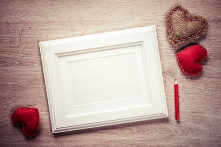 White photo frame small red hearts and pencil on wooden table