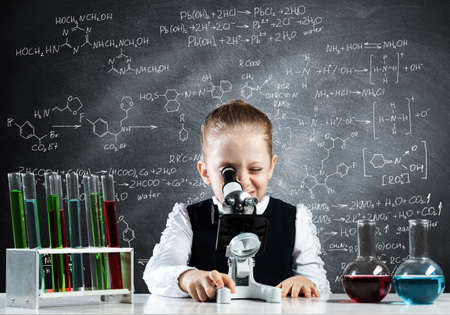 Little girl scientist looking through microscope in classroom at chemistry lesson. School chemical laboratory with glass flasks and test tubes. Schoolgirl making experiment in chemistry class.の写真素材