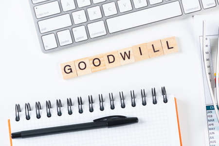 Goodwill message with letters on wooden cubes. Still life of workspace with supplies. Flat lay white surface with computer keyboard and spiral notebook. People greeting phrase and motivation.の写真素材