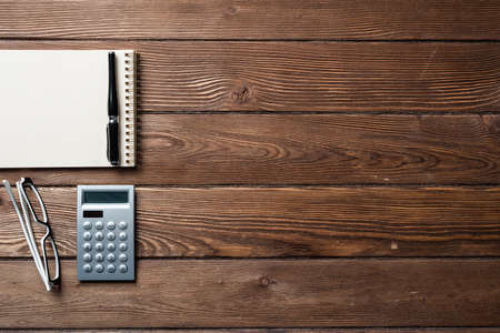 Still life of accountant workspace with office accessories. Flat lay wooden desk with elegant glasses, calculator and spiral notepad. Accounting and banking services. Finance and investment concept.の写真素材