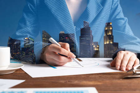 Corporate consultant analyze financial analytics. Double exposure concept with woman hands and modern skyscrapers. Analyst in suit working at workplace in office. Real estate investment company.の写真素材