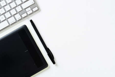 Top view of modern working place. Graphic tablet, pen and computer keyboard on white surface....
