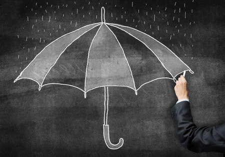 Businessman hand with chalk draws umbrella sketch on chalkboard. Freehand illustration on blackboard. Public insurance program advertisement. Protection against various life and economic risks.の写真素材