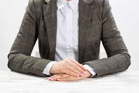 Close up businesswoman sitting at desk with folded arms. Concentrated business lady on background of white wall. Business consultation in office. Corporate woman in suit posing at her workplace.の写真素材