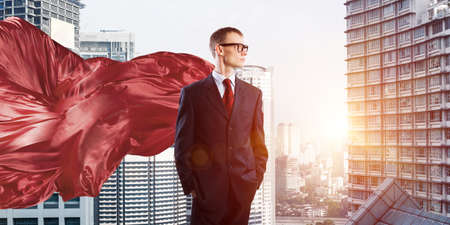 Young confident businessman wearing red cape against modern city backgroundの写真素材