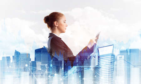 Young businesswoman with tablet computer on modern cityscape background. Double exposure concept with beautiful woman in business suit. Digital technology in stock trading and real estate investmentの写真素材