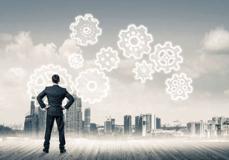 Back view of businessman looking at modern city and drawn gear mechanismの写真素材