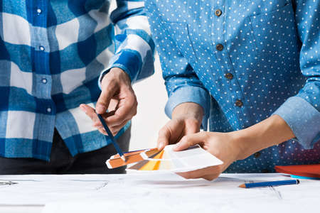 Interior designers discussing color samples for design project. Close up man hand with pencil pointing on color palette. Professional building, decoration and renovation. Teamwork and creativityの写真素材
