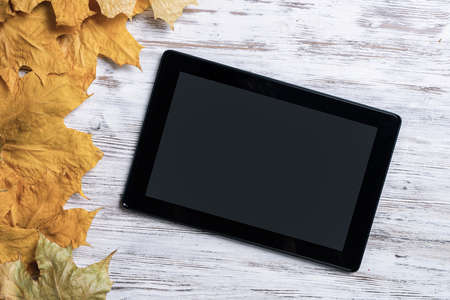 Tablet computer with blank screen lies on vintage wooden desk with bright foliage. Flat lay...