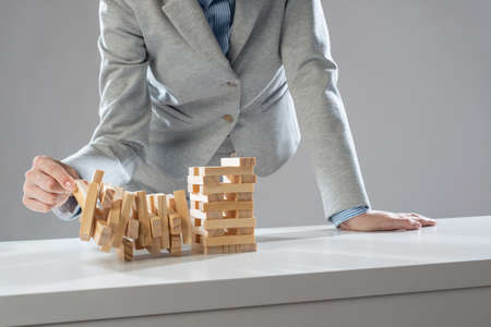 Businesswoman removing wooden block from falling tower on table. Management of risks and economic instability concept with wooden game. Failure and collapse in corporate businessの写真素材