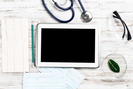 Laboratory patient examination in doctors office. Top view tablet computer, medical mask, stethoscope and cardiogram on wooden desk. Medical diagnostics and examination in modern hospital.の写真素材
