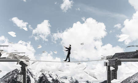 Businessman walking blindfolded on rope among flying paper planes and above huge gap in bridge as symbol of hidden threats and risks. Nature view on background. 3D rendering.の写真素材