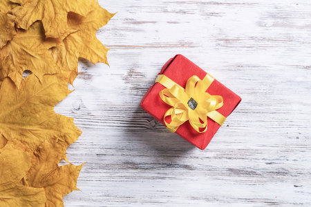 Bright autumn composition with gift box and yellow maple leaves. Holiday present decorated yellow ribbon bow lies on vintage wooden desk. Happy thanksgiving congratulation. Autumn sale advertising.の写真素材