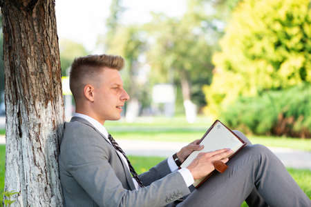 businessman in the park sits near a tree and looks through the diary. work in natureの写真素材