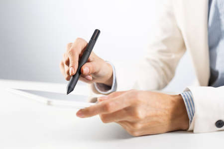 Man in business suit using tablet computer. Close-up of male hands holding pen and tablet gadget. Businessman at workplace in office. Business occupation and mobility, internet smart technology in jobの写真素材