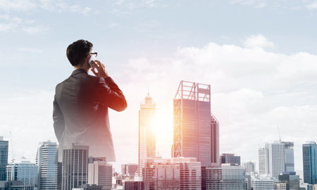 Double exposure of elegant businessman standing with back and talking his mobile phoneの写真素材