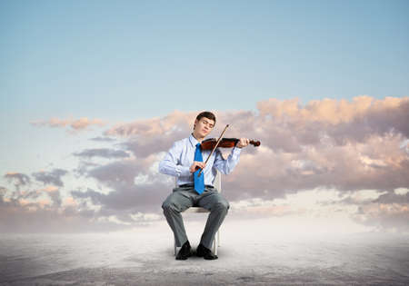 Young businessman plays the violin and enjoys the music. sits on a chairの写真素材