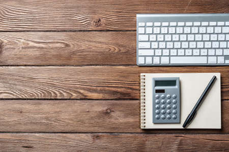 Still life of accountant workspace with office accessories. Flat lay old hardwood desk with computer keyboard, notepad and calculator. Accounting and banking services. Finance and investment concept.の写真素材