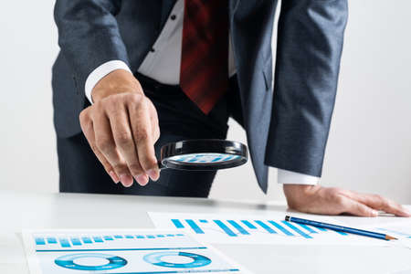 Businessman analyzing financial documents with magnifying glass in hand. Financial expertise and...