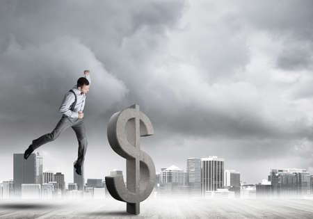 Young furious businessman going to crash with fist stone dollar symbolの写真素材