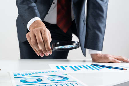 Businessman analyzing financial documents with magnifying glass in hand. Financial expertise and...