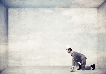 Young handsome businessman wearing white paper crown running in a hurryの写真素材