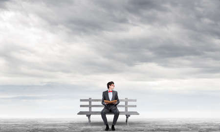 Student sits on a bench, holding a book. Traditional education conceptの写真素材