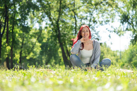 Portrait of a young attractive woman. Sitting in the park on the grass cross-legged