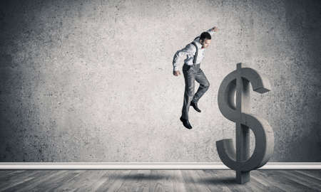 Young furious businessman going to crash with fist stone dollar symbolの写真素材