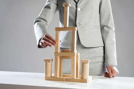 Business woman building tower on table from wooden blocks. Business development and assistance...