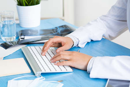 Close-up of female doctor hands typing at computer keyboard. Physician in medical uniform working at desk. Examination and diagnosis in hospital. Practitioner workplace with computer keyboard.の写真素材
