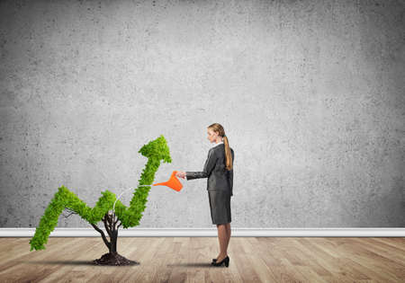 Young attractive businesswoman watering plant in ground with canの写真素材