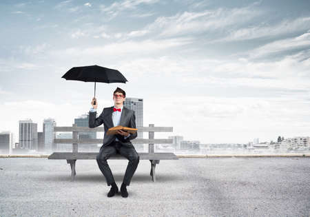 Young student with a book and umbrella sits on a wooden benchの写真素材