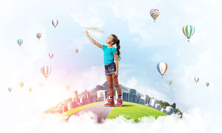 Cute kid girl on city floating island throwing paper planeの写真素材