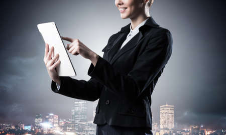 Businesswoman using tablet computer. Double exposure concept with night city and woman in business suit. Real estate investment. Digital technology in property management and development company.の写真素材