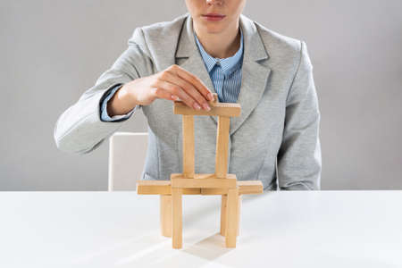Business woman building tower on table from wooden blocks. Business development and assistance concept. Young woman wearing formal wear sitting in office interior. New challenge and leadershipの写真素材