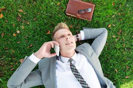 businessman lies on the grass and talks on the phoneの写真素材