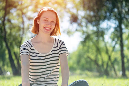 Portrait of a young attractive woman. Sitting cross-legged in the parkの写真素材