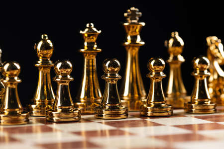 Golden chess figures standing on chessboard. Intellectual and tactic game. Strategy planning, leadership and teamwork business concept. Close-up gold chess pieces in row on black background.の写真素材