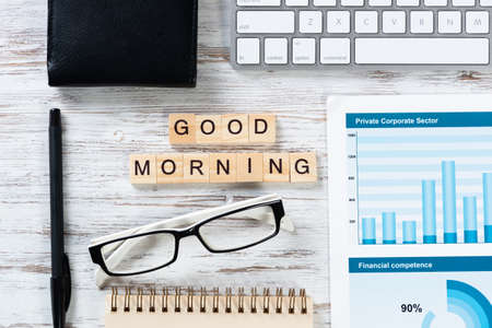 Good morning message with letters on wooden cubes. Still life of workspace with supplies. Flat lay wooden desk with computer keyboard and spiral notebook. Morning greeting phrase and motivation.の写真素材