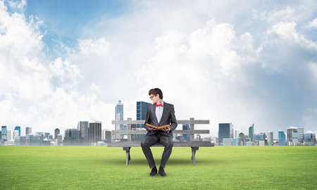 Young student sits on a wooden bench with a bookの写真素材